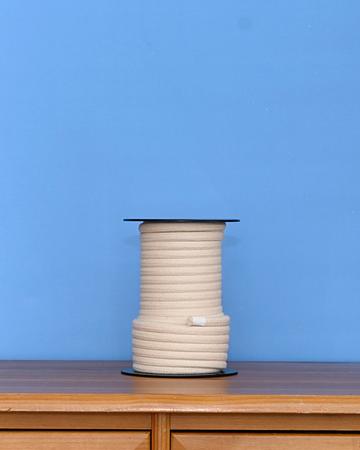 Large spool of off-white organic cotton rope on a wooden surface against a blue wall.