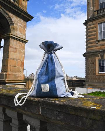 Blue and white striped cotton drawstring bag with a Rita Blu Studio logo tag on a stone balcony.