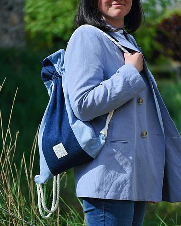 Hands holding a blue and navy sustainable fabric drawstring bag against a clear sky.