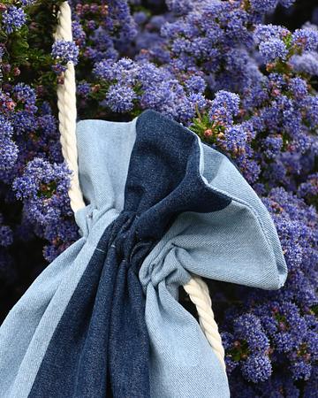Two-tone blue denim drawstring bag hanging against a background of purple lavender-colored flowers.