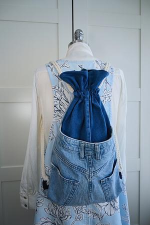 Blue denim drawstring bag worn over a floral light blue dress on a mannequin.