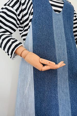 Mannequin wearing a two-tone blue patchwork denim pinafore dress over a black and white striped long sleeve shirt.