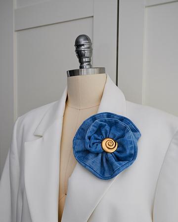 A handcrafted rose-shaped brooch made from reclaimed denim with a vintage button centrepiece.
