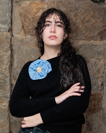 A handcrafted rose-shaped brooch made from reclaimed denim with a vintage button centrepiece.