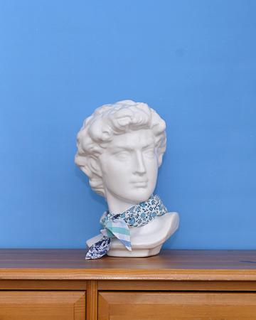 White marble bust wearing a blue and white floral patterned scarf on a wooden surface against a blue wall.