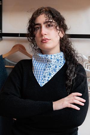 Young woman with curly hair wearing a black sweater and a blue floral print checkered neck scarf.